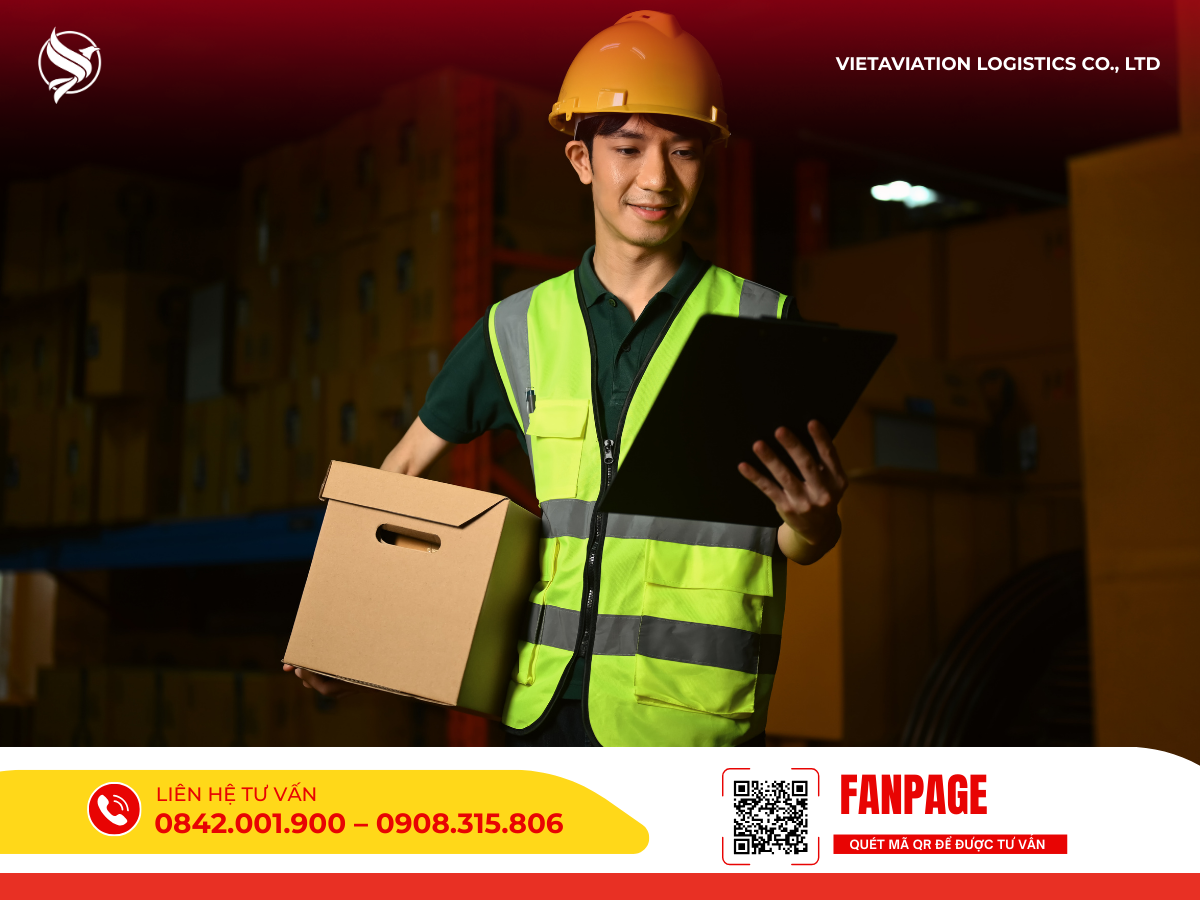 Hình ảnh một nam nhân viên kho mặc áo phản quang và đội mũ bảo hộ đang ôm một thùng carton bằng một tay và tay kia cầm bìa hồ sơ để kiểm tra thông tin.