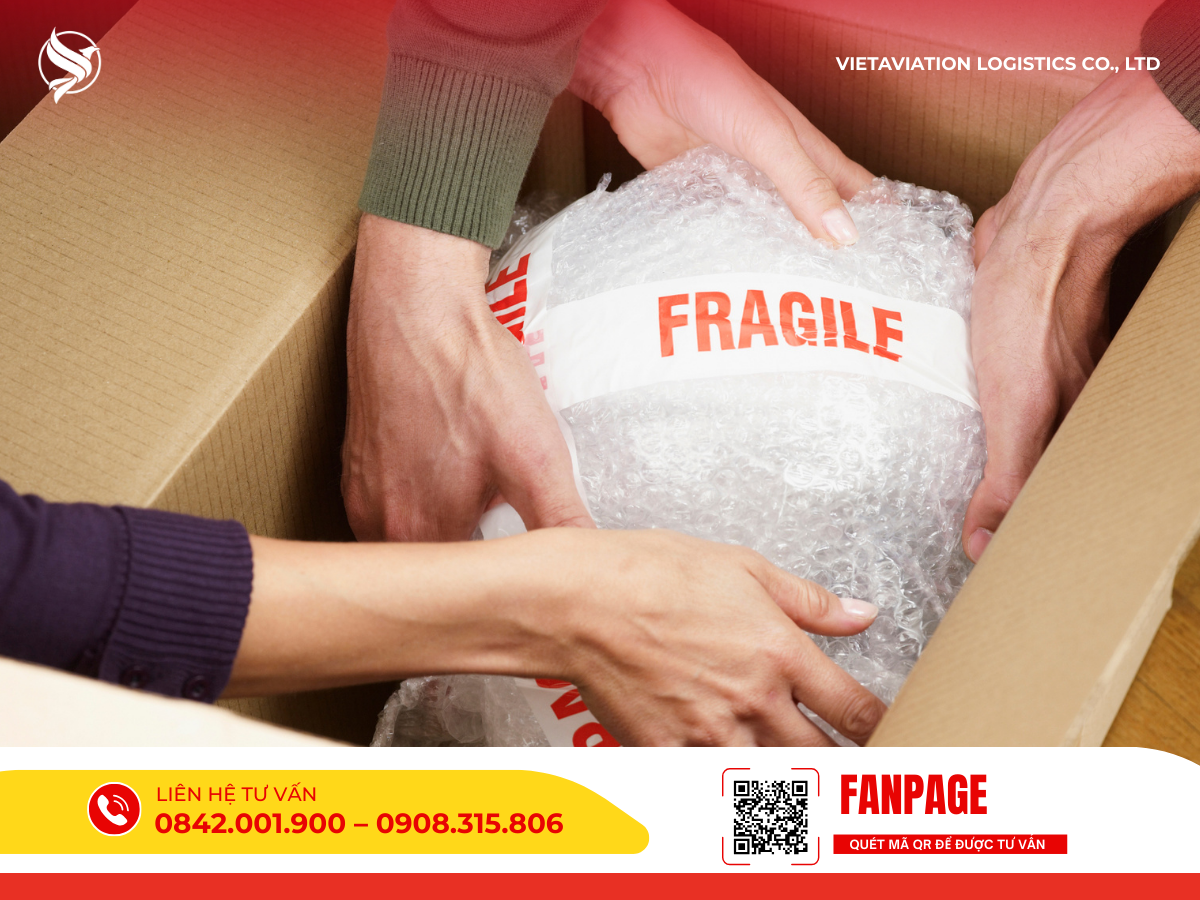 Hình ảnh hai người đang cẩn thận dùng tay đặt một kiện hàng đã được bọc kín bằng màng xốp hơi chống sốc và dán băng keo cảnh báo FRAGILE màu đỏ vào bên trong thùng carton.