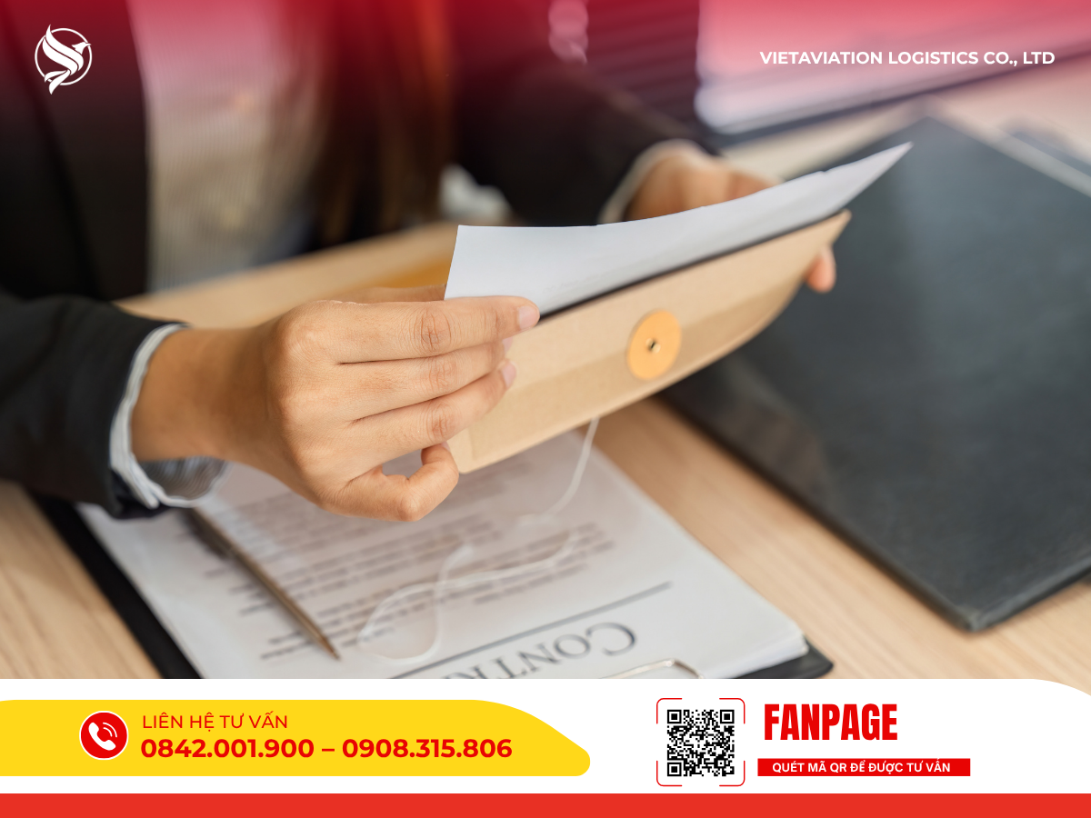 Hình ảnh cận cảnh đôi tay đang cẩn thận mở chiếc phong bì hồ sơ màu nâu có cúc buộc dây, bên trong chứa tài liệu giấy trắng, được đặt trên bàn làm việc cùng với bút và một tập giấy tờ hợp đồng.