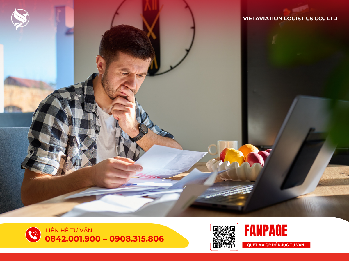 Hình ảnh người đàn ông đang ngồi trước máy tính xách tay, vẻ mặt tập trung xem xét và đối chiếu các giấy tờ trên tay.